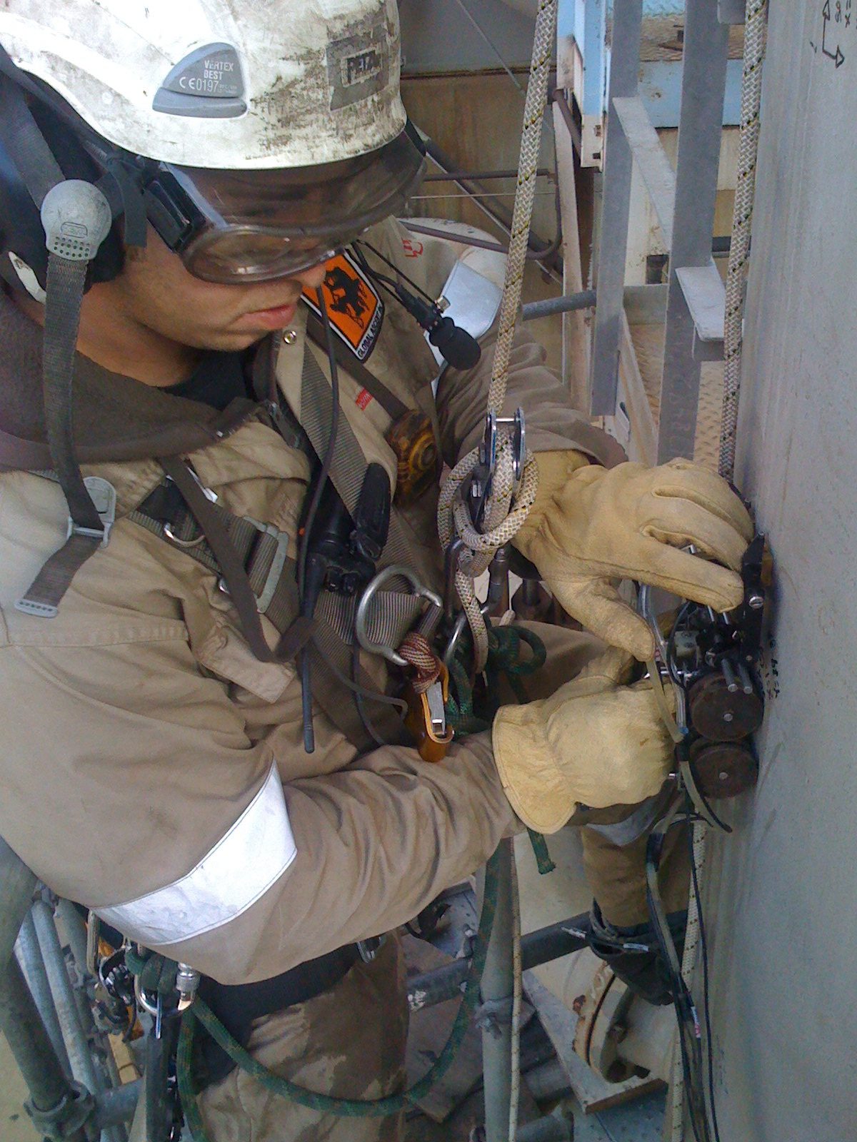 Worker in safety gear climbing industrial structure.