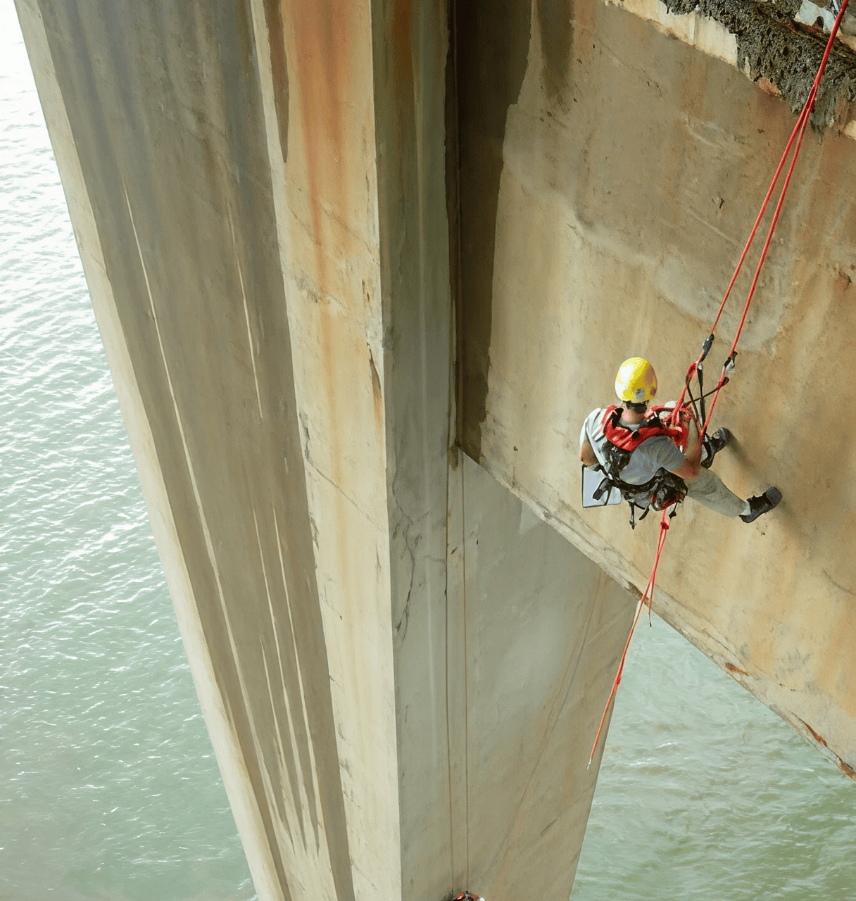 Worker abseiling down a bridge structure.