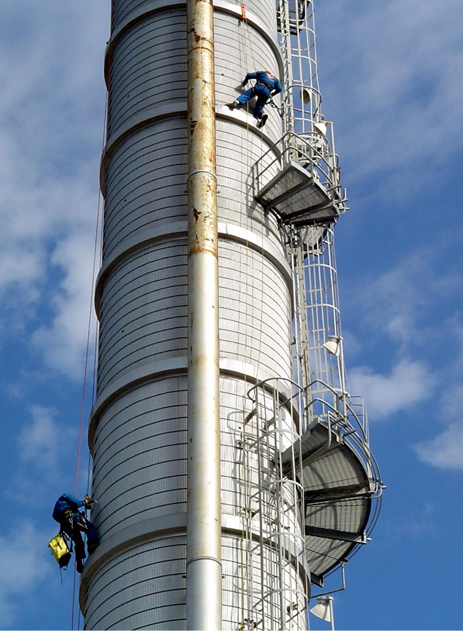Workers climbing a tall industrial chimney structure.