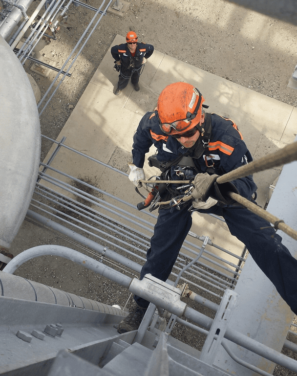 Worker climbing industrial structure with rope.