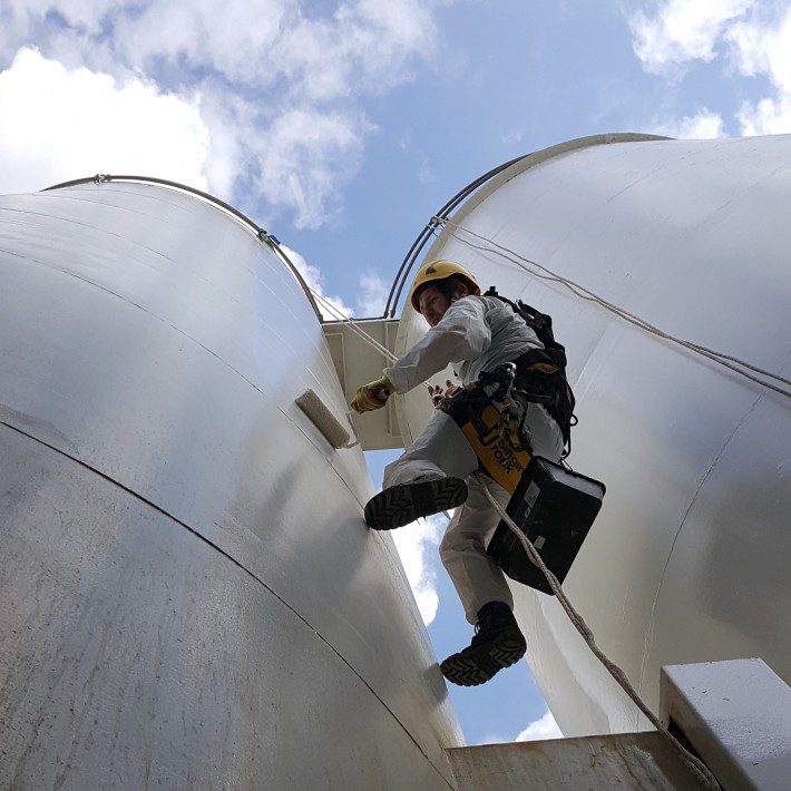Worker climbing large industrial tanks.